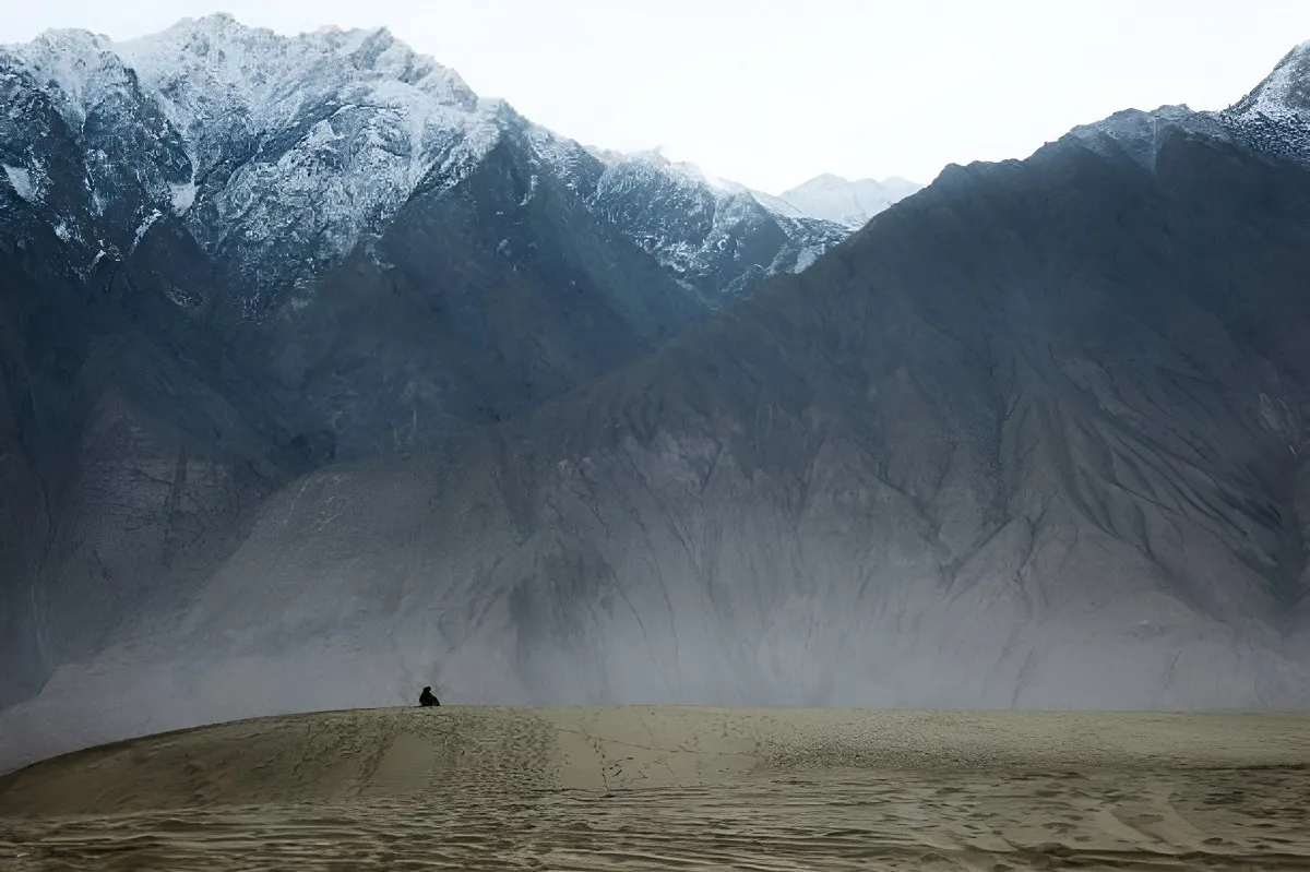 The alone man sitting on the sand dune in Cold Katpana Desert in Karakoram mountains at the sunset